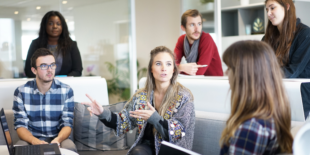 woman explain an idea on a sofa with 5 people listening to her intently 